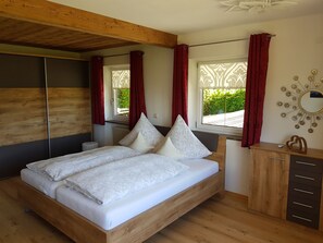 Quarto com cama de madeira, cômoda, espelho e janela com cortinas vermelhas.