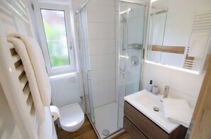 A bathroom with a toilet, a shower enclosure, and a vanity with a mirror. - Kälbersteinstüberl Vacation Rental (Bischofswiesen)