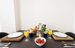 Et morgenbord med to tallerkener, en skål jordbær, to glas appelsinjuice, en kurv med bagværk og en vase med blomster.