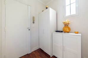 Ein Flur mit weißen Türen, Holzboden, einem weißen Schrank mit einer Vase und einer Schüssel darauf sowie einer Wandleuchte.