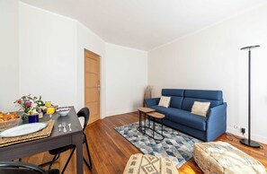 Ein modernes Wohnzimmer mit einem blauen Sofa, einem Esstisch mit Frühstücksgebäck und einer stehenden Stehlampe.