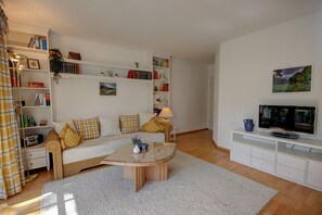 A living room with a sofa, coffee table, TV, and bookshelves. - Vacation rental for 2 people with a balcony, 50 m² (Inzell)