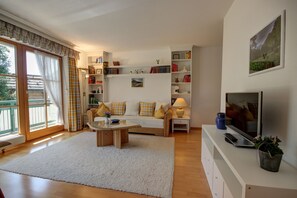 A living room with a sofa, coffee table, TV, and bookshelves. - Vacation rental for 2 people with a balcony, 50 m² (Inzell)