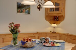 A dining table with a blue checkered tablecloth, a vase with flowers, a basket of pretzels, a plate with sliced meats, a jar of jam, and a candle holder. - Vacation rental for 2 people with a balcony, 50 m² (Inzell)