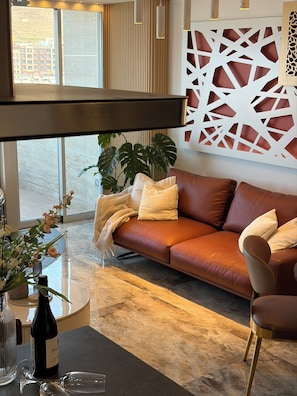 A modern living room with a leather sofa, a glass coffee table, and a decorative wall panel. - Larimar Luxury Seafront Apartment with Jacuzzi (Iż-Żebbuġ)