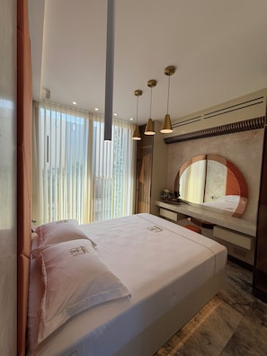 A hotel room with a bed, a vanity with a mirror, and a window with curtains. - Larimar Luxury Seafront Apartment with Jacuzzi (Iż-Żebbuġ)