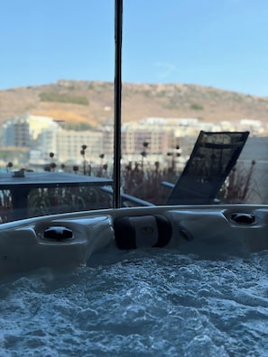A hot tub with a view of buildings and a hill in the background. - Larimar Luxury Seafront Apartment with Jacuzzi (Iż-Żebbuġ)