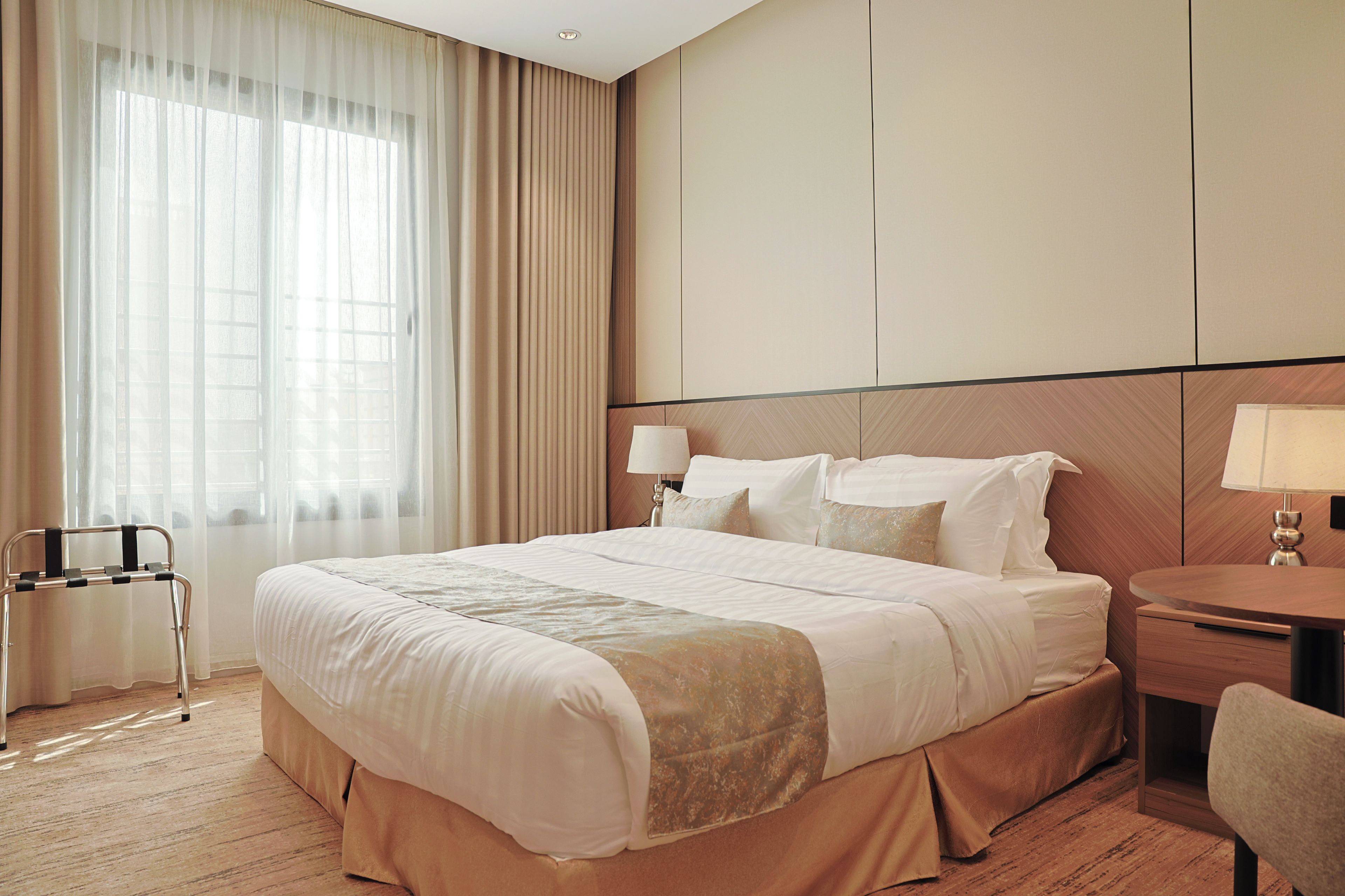 Een hotelkamer met een groot bed, een nachtkastje, een stoel en een raam met gordijnen.