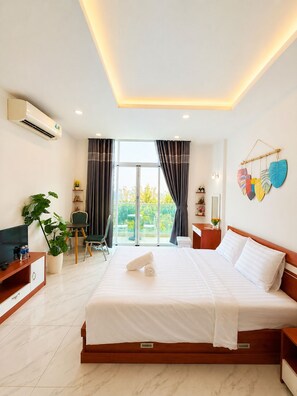 A hotel room with a large bed, a TV, a plant, and a view of the outdoors.