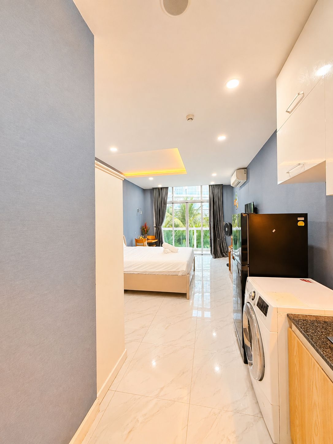 A hotel room with a bed, a washing machine, a TV, and a window with curtains.