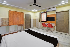 Habitación de hotel con cama, escritorio, dos sillas, armario y aire acondicionado.