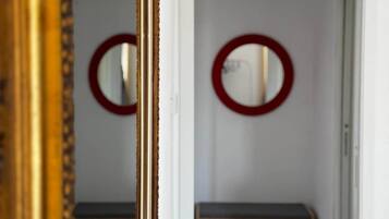 Un corridoio con uno specchio che riflette una stanza, una panca e una porta.