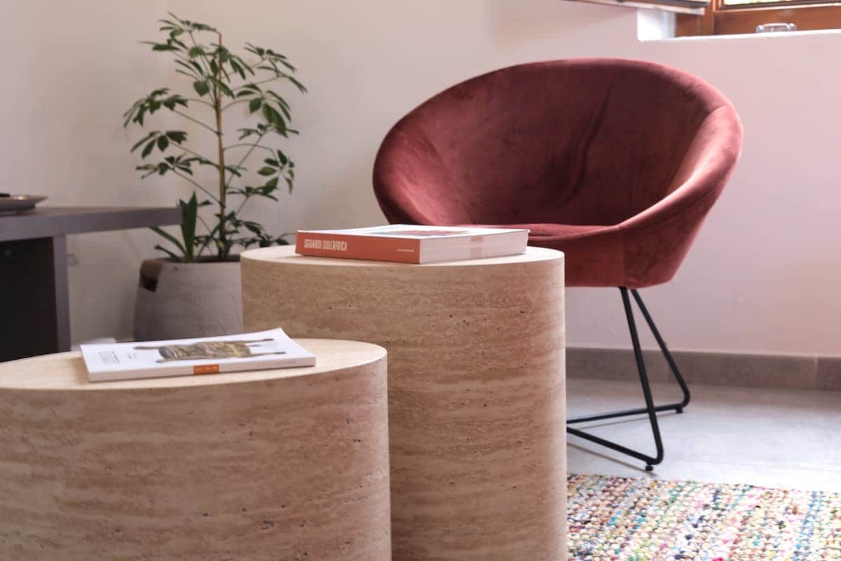 A room with a red chair, a potted plant, and a small round table with a book on it.