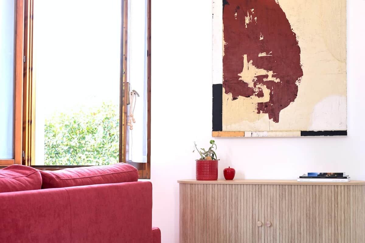 Une pièce avec un canapé rouge, un meuble en bois et un grand tableau abstrait accroché au mur.