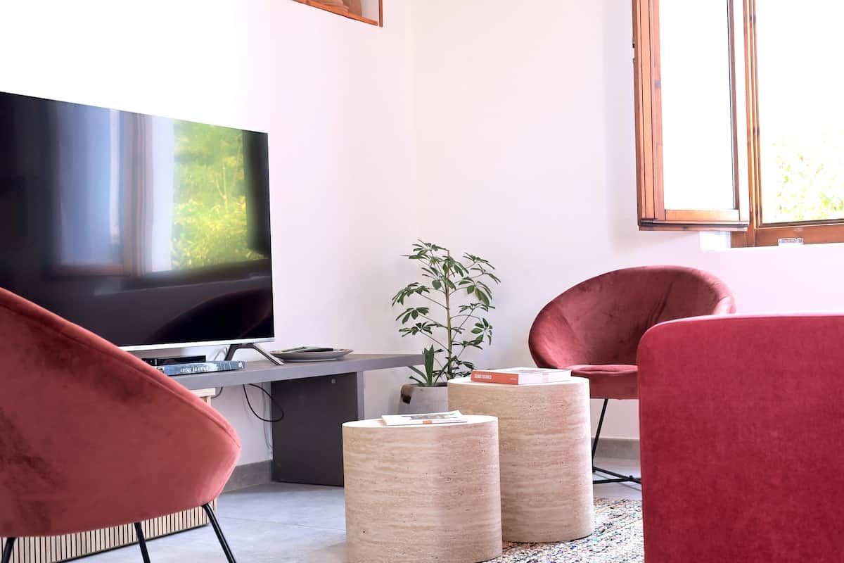 Un salon moderne avec un téléviseur à écran plat, des fauteuils rouges, une petite table et une plante en pot.
