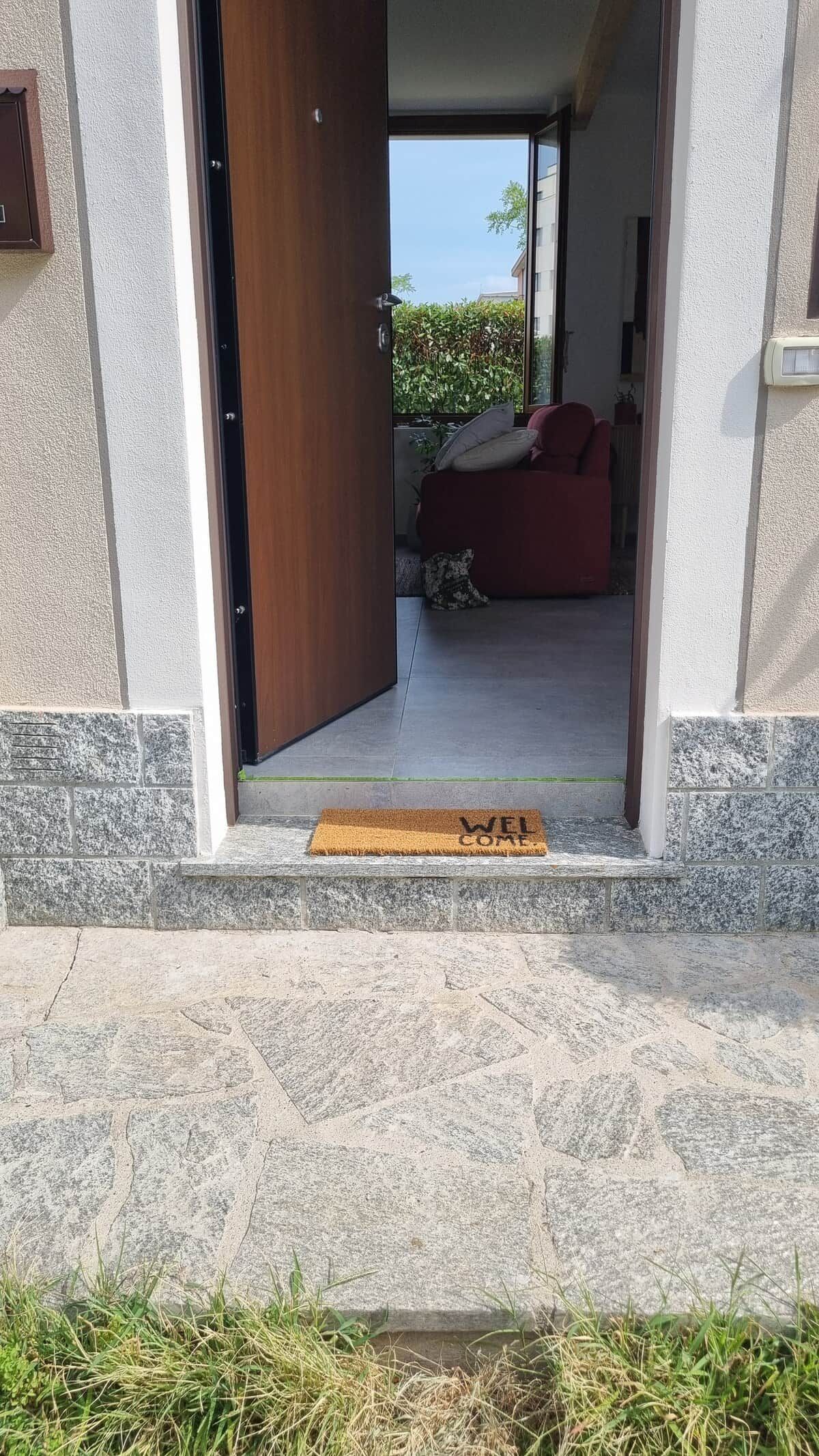 Un passage donnant sur une pièce où se trouvent un canapé rouge, une porte en bois et un paillasson.