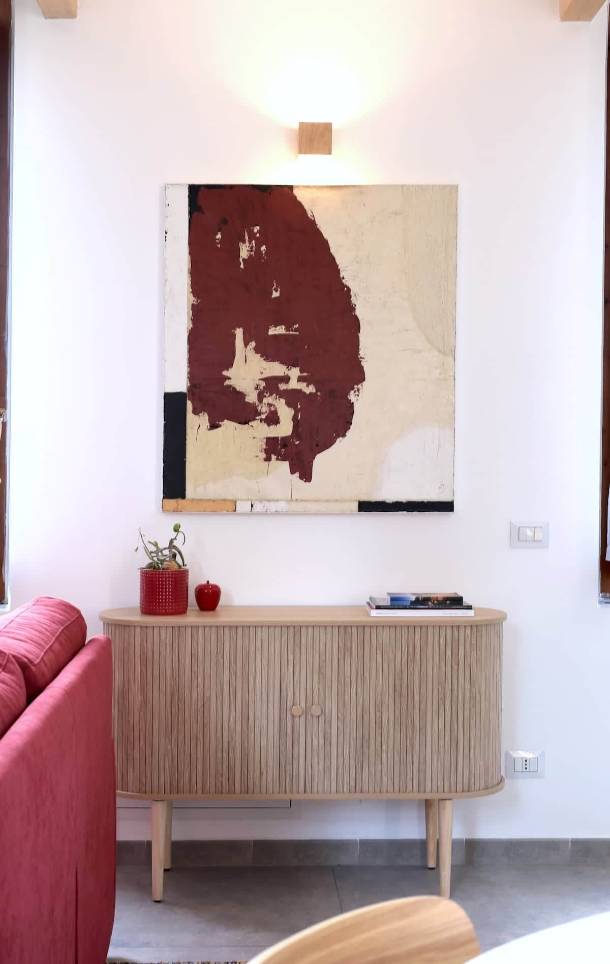 Una stanza con un armadio in legno, un divano rosso e un quadro astratto appeso al muro.