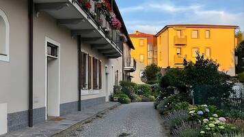 Une ruelle étroite, bordée d’immeubles dont les balcons sont ornés de fleurs, mène à un bâtiment jaune dont l’entrée est bien visible.