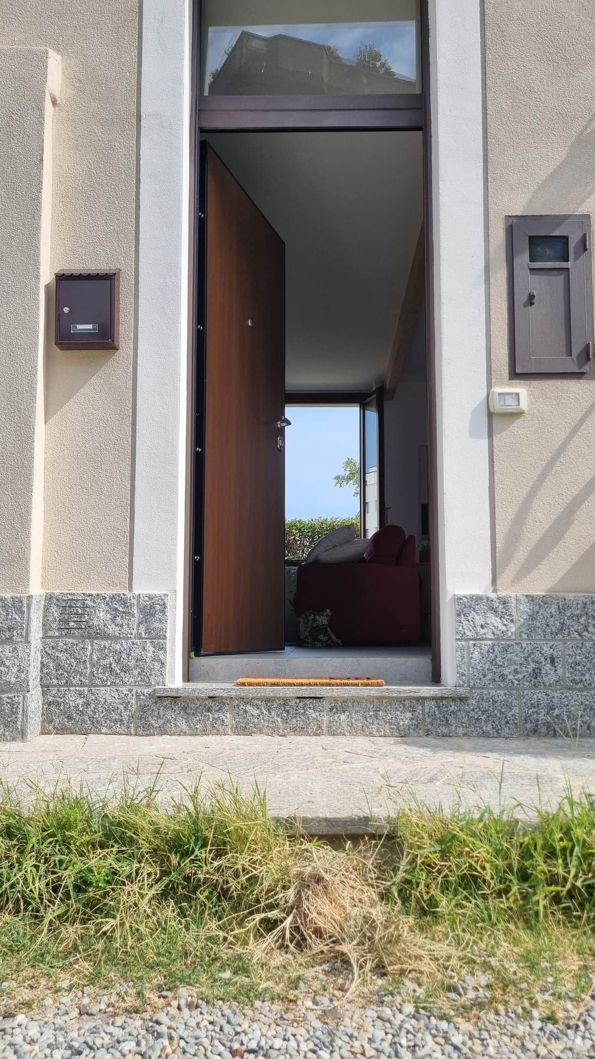 Un ingresso che dà su una stanza con una sedia rossa e un tavolino, una finestra con vista e una porta con maniglia.