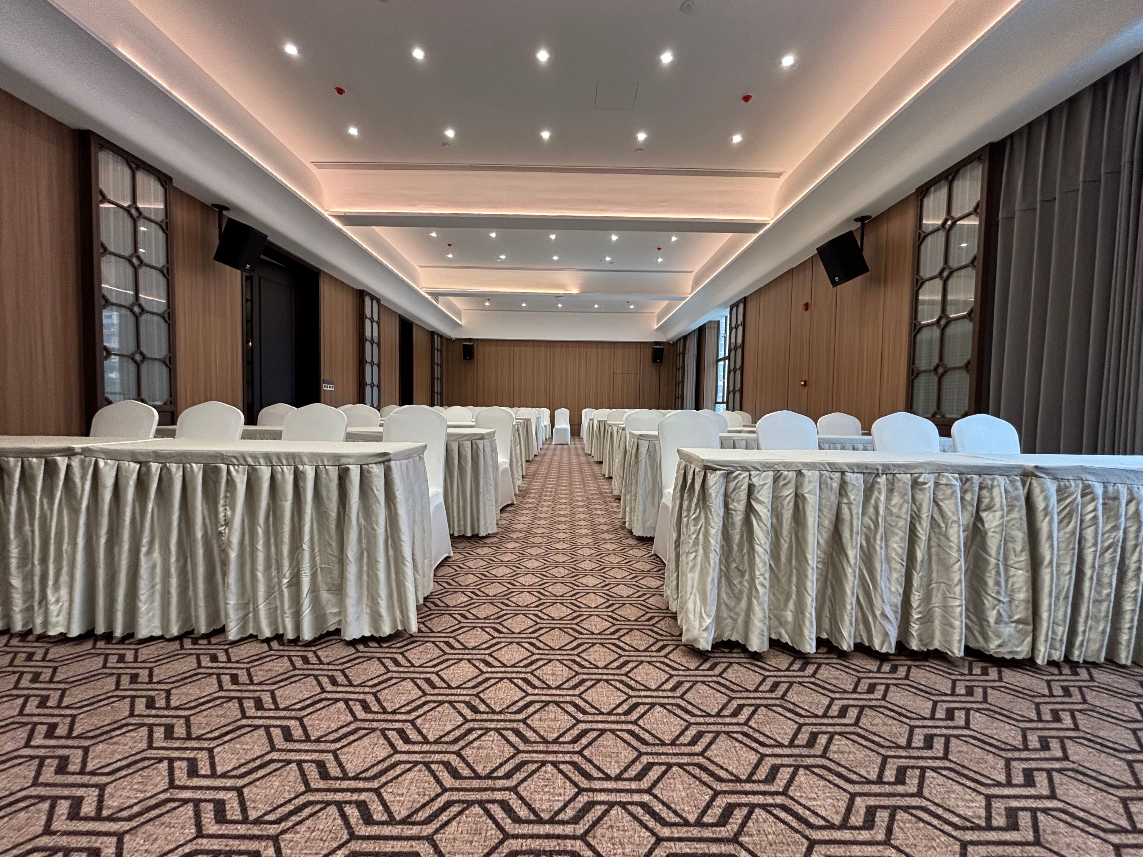 Un salón de conferencias con filas de mesas y sillas, alfombra estampada e iluminación empotrada.