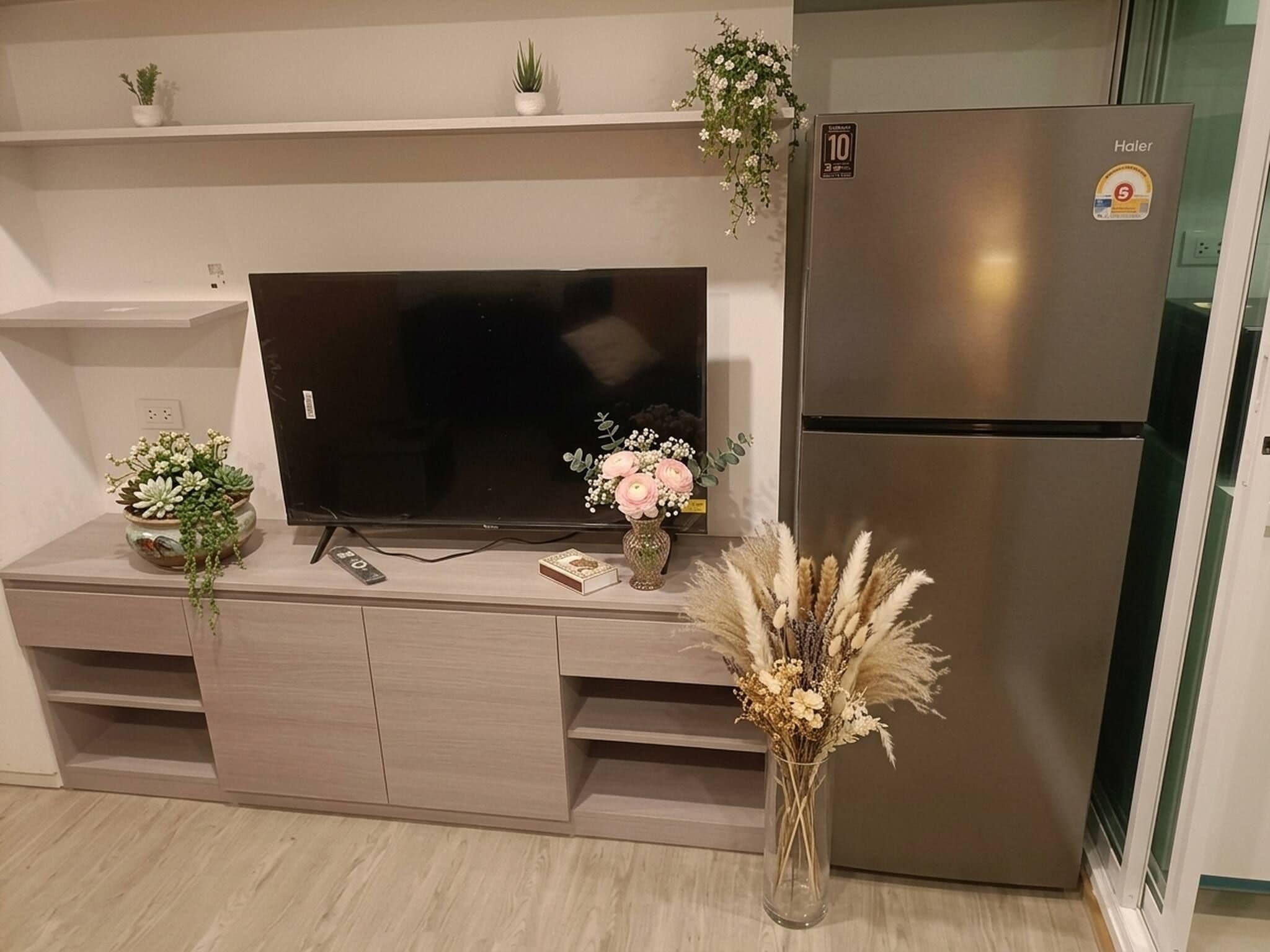 A modern kitchen with a built-in TV, a stainless steel refrigerator, and decorative plants.