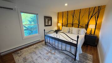 A bedroom with a bed, a window, a wall with a tree mural, and a nightstand with a lamp.