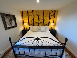 A bedroom with a bed, two bedside tables, a nightstand, a wall-mounted picture, and a patterned wall. - Serene Sunrise Long Range Mountain View 1-bedroom home in charming Blowing Rock (Blowing Rock)