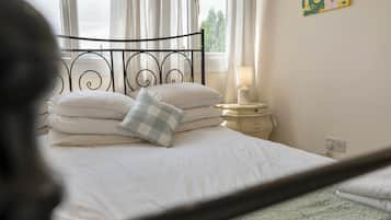 A bed with white bedding and a checkered pillow, a bedside table with a lamp, and a window with curtains.