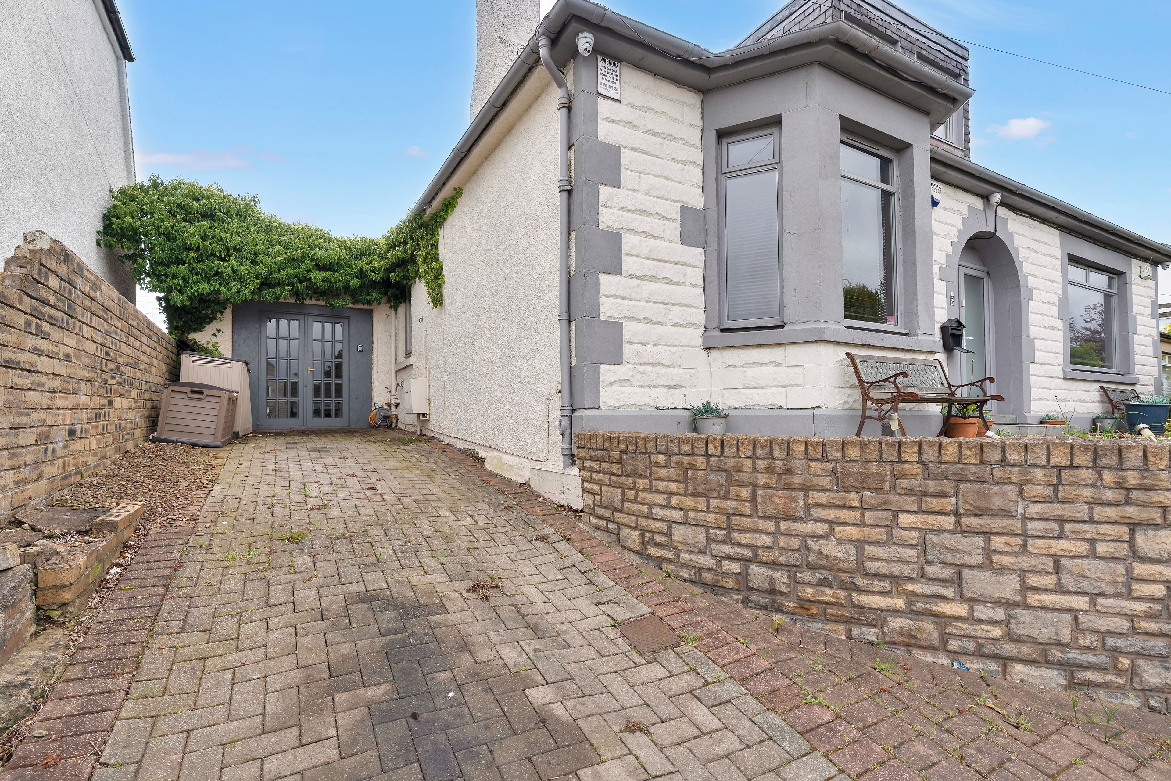 A residential property with a paved driveway, a brick wall, and a window with shutters.