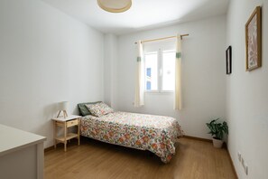 A bedroom with a bed, bedside table, lamp, window with curtains, and a potted plant. - DA CESAR | Spacious Stay near Maspalomas (El Tablero)