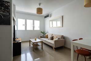 A modern living room with a sofa, a coffee table, a dining table with chairs, and a large window providing natural light. - DA CESAR | Spacious Stay near Maspalomas (El Tablero)
