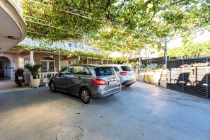 Ein Parkplatz mit zwei Autos und einem Motorrad, ein Gebäude mit einer Stein-Fassade und ein Baum mit grünen Blättern.
