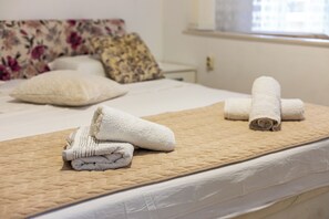 Ein ordentlich gemachtes Bett mit gesteppter Bettdecke, einem Kopfkissen und gerollten Handtüchern.