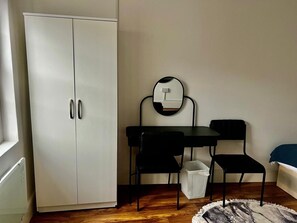 A room with a white wardrobe, a small table with two chairs, a mirror, and a waste bin. - Apartment Sleeps 2 With Wifi (London)
