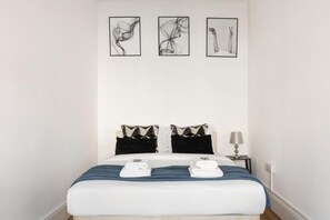 Habitación de hotel con una cama, dos almohadas, una mesita de noche con lámpara y tres cuadros enmarcados en la pared.