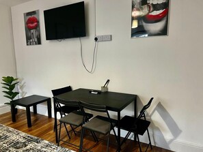 A room with a dining table, chairs, a TV mounted on the wall, and a power outlet. - Apartment Sleeps 2 With Wifi (London)