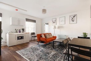 Una cocina moderna con armarios blancos, un comedor con mesa y sillas, y una sala de estar con sofá y alfombra.