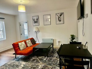 En moderne stue med sofa, spisebord og billedkunst på væggen.