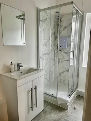 Un baño con ducha envuelta en vidrio, un lavamanos blanco con dispensador de jabón y un espejo sobre el lavamanos.
