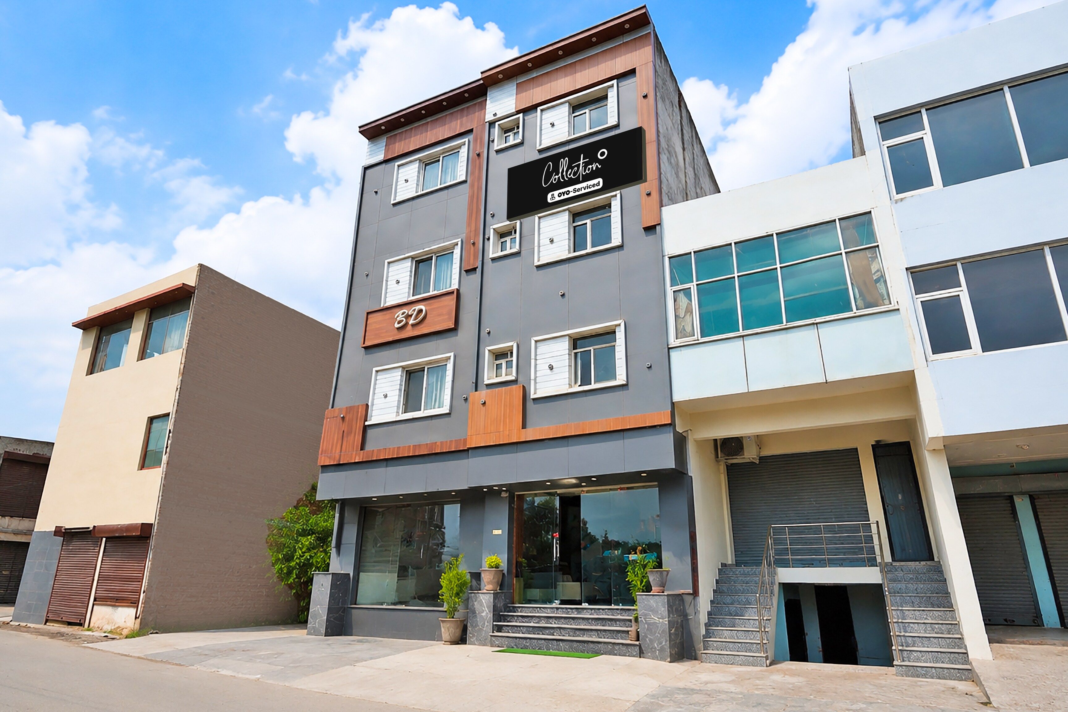 Un edificio de varios pisos con fachada moderna, que cuenta con un llamativo letrero 'BD' en la planta baja, un cartel de 'Collection' sobre la entrada y una escalera que conduce a la entrada principal.