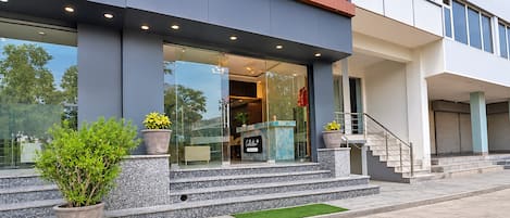 A modern building with a glass entrance, outdoor seating, and a staircase leading to the entrance.