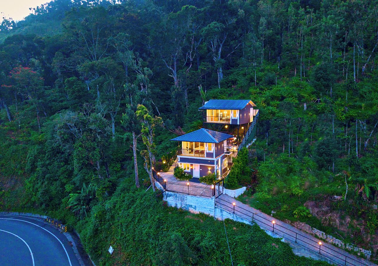 Ein zweistöckiges Haus mit Balkon, umgeben von dichtem Wald, mit einem gepflasterten Weg zum Eingang.