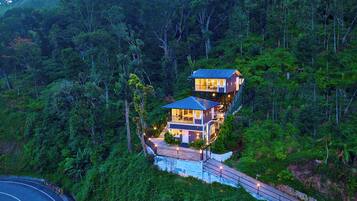 Ein zweistöckiges Haus mit Balkon, umgeben von dichtem Wald, mit einem gepflasterten Weg zum Eingang.