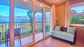 Ein Balkon mit einer Couch und Stühlen, großen Schiebeglastüren und Blick auf Berge.