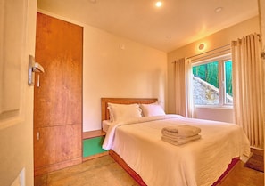 Un dormitorio con cama, armario, ventana con cortinas y vistas a zonas verdes.