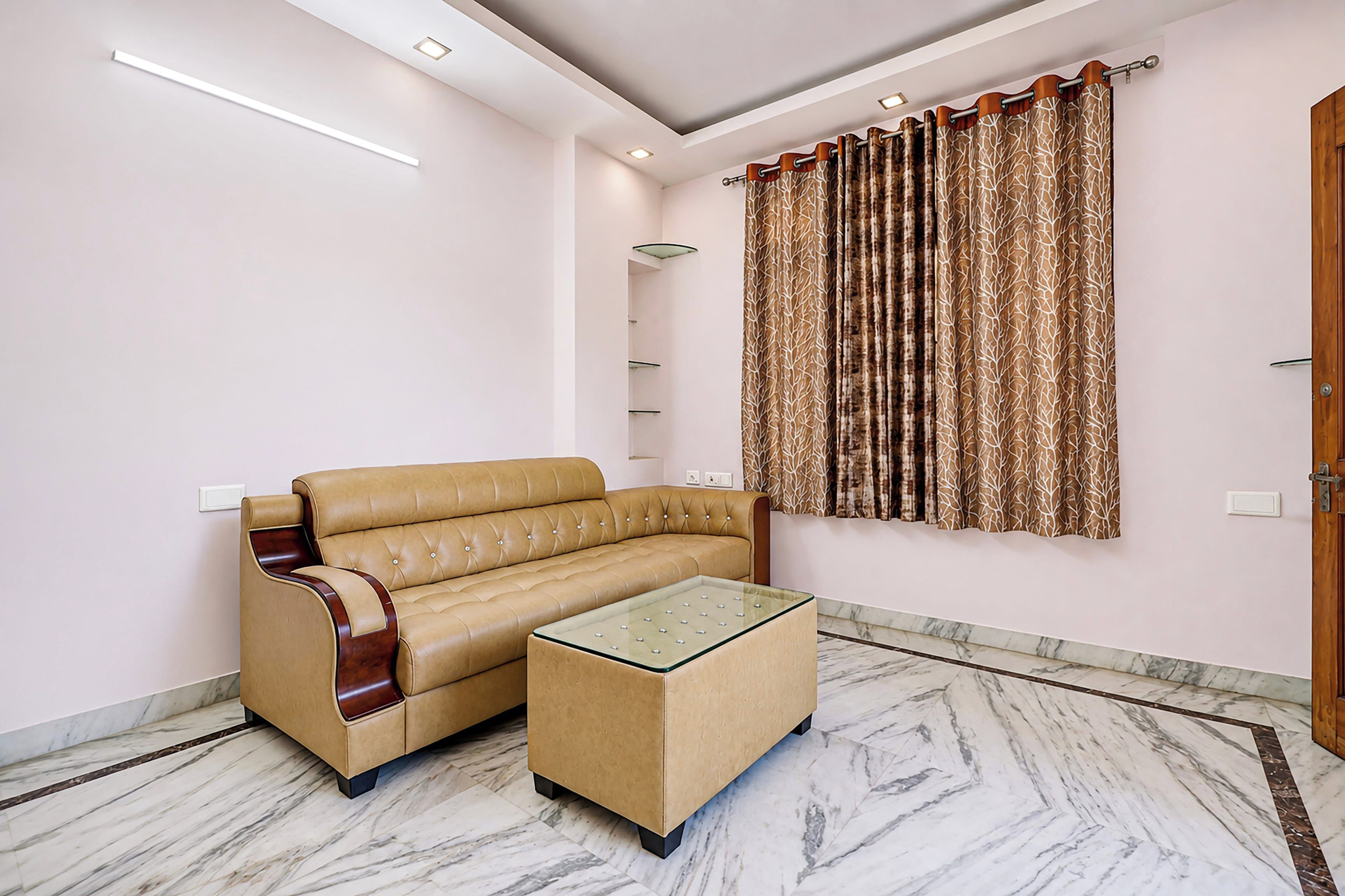 A modern living room with a beige sofa, a glass coffee table, and a patterned curtain.