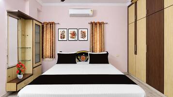 A bedroom with a bed, a ceiling fan, an air conditioning unit, a wardrobe, a mirror, and a window with curtains.
