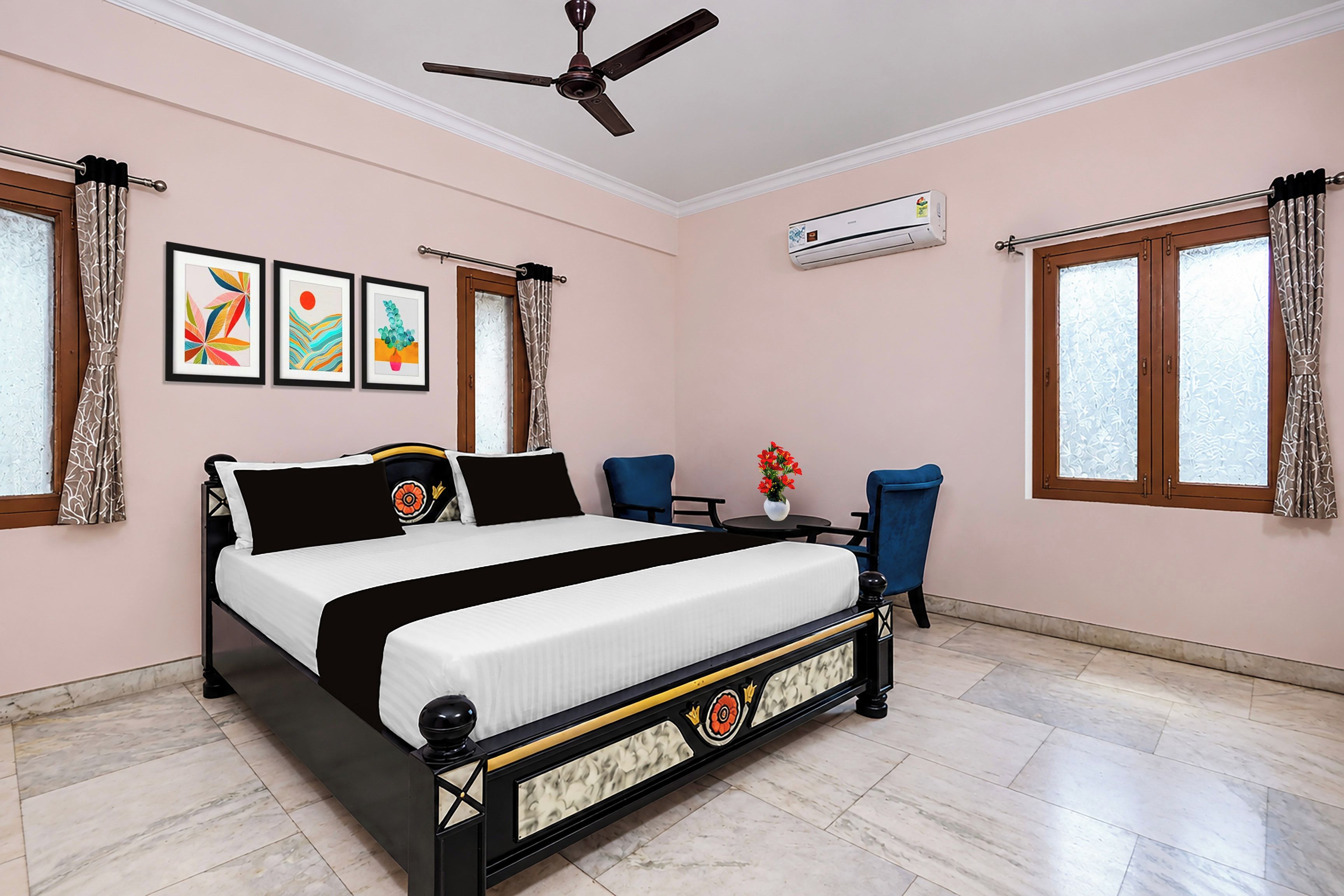 A bedroom with a bed, a ceiling fan, a window with curtains, an air conditioning unit, and a small table with a vase of flowers.