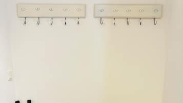 Een hoek van een kamer met een betegelde vloer, een witte, structuurwand en twee wandhaakjes met genummerde labels.