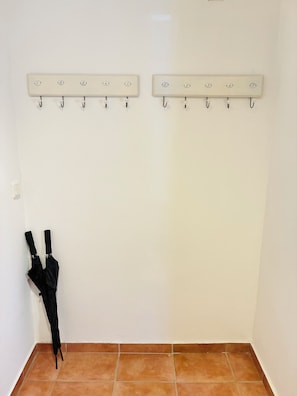 A corner of a room with a tiled floor, a white textured wall, and two wall-mounted coat hooks with numbered labels.